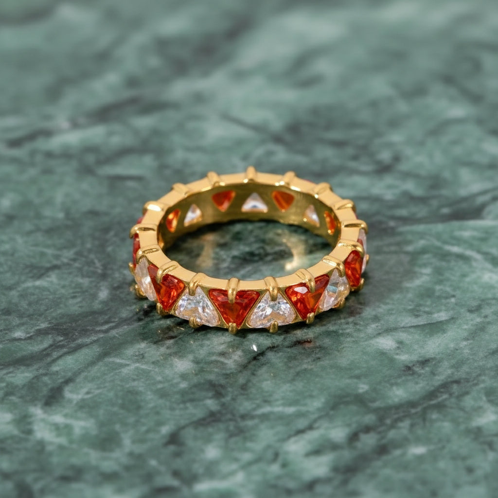 Goldring mit roten und klaren Edelsteinen auf einer grünen Marmoroberfläche