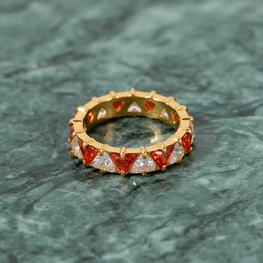 Goldring mit roten und klaren Edelsteinen auf einer grünen Marmoroberfläche