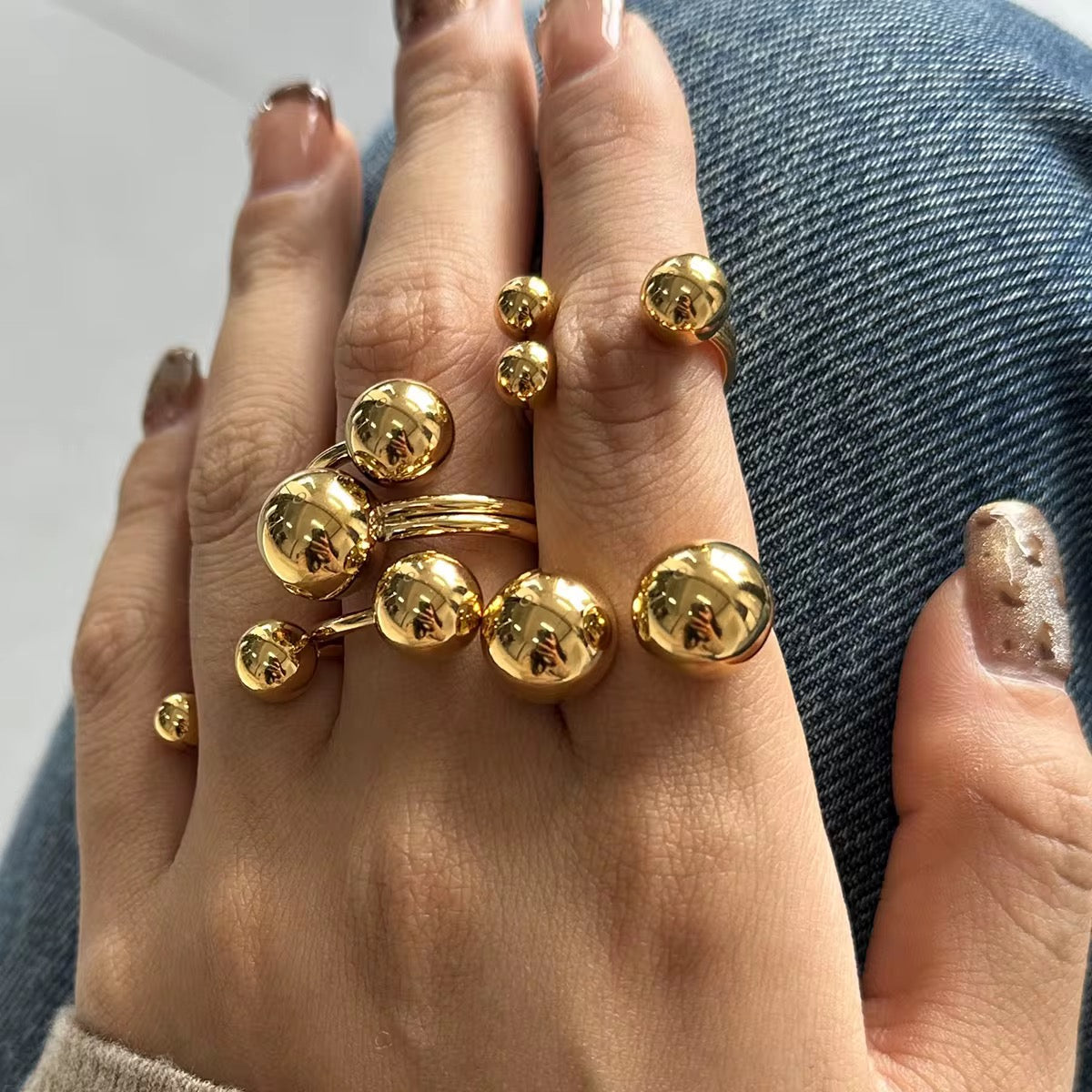 A gold-plated stainless steel ring with multiple ball shapes on a person's finger.