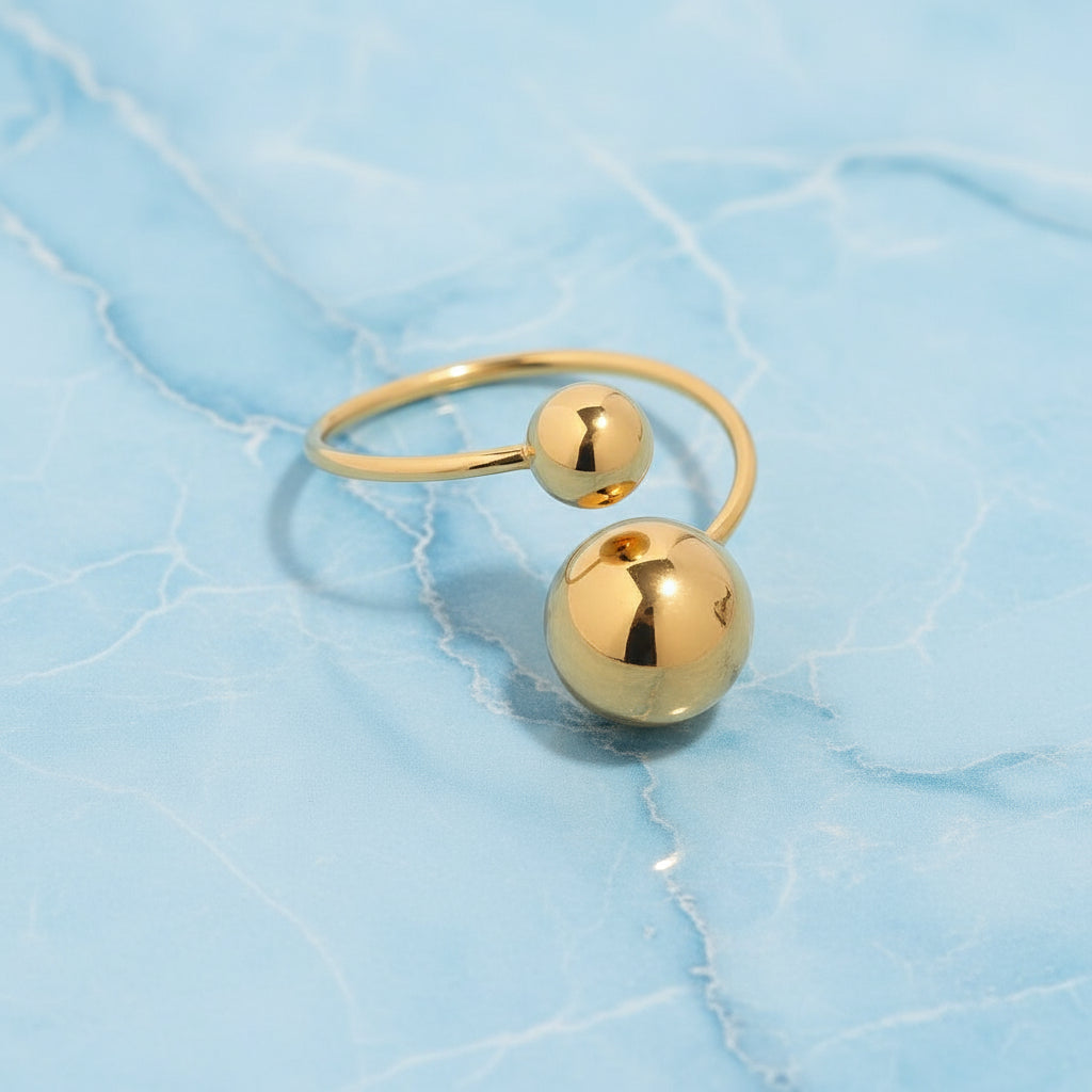 Goldring mit zwei kugelförmigen Perlen auf hellblauem Marmorhintergrund