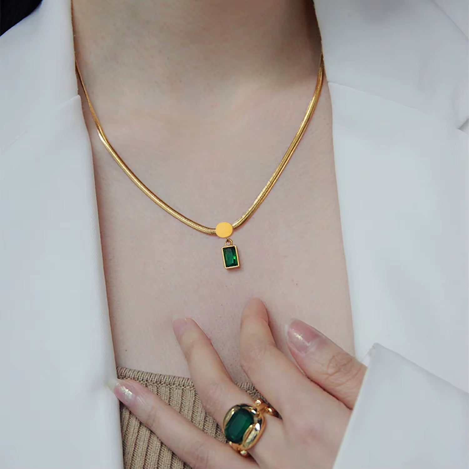 Eine Frau, die eine vergoldete Edelstahl-Schlangenkette mit einem Anhänger mit einem grünen Zirkonstein trägt.