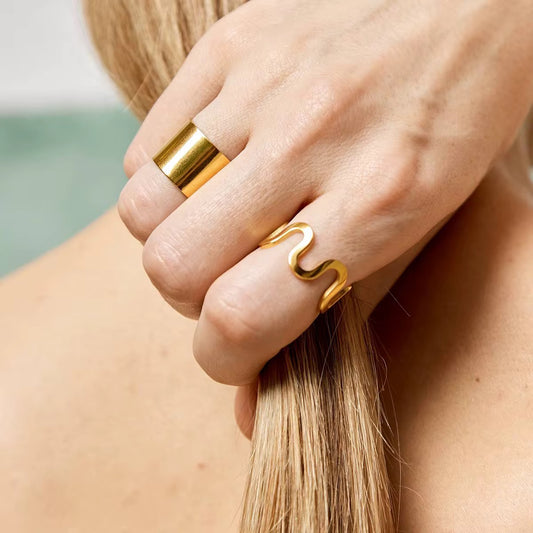 Nahaufnahme einer Frauenhand, die einen vergoldeten Edelstahlring mit geometrischem Design trägt.